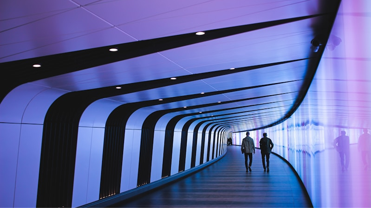 Two men walking down a long, curved hallway lit in blueish purple.