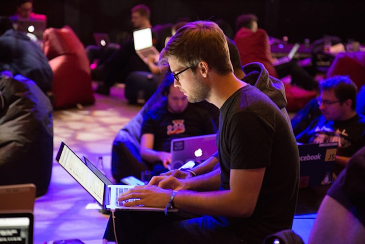 A man sitting on the ground working on a laptop with others around him doing the same.